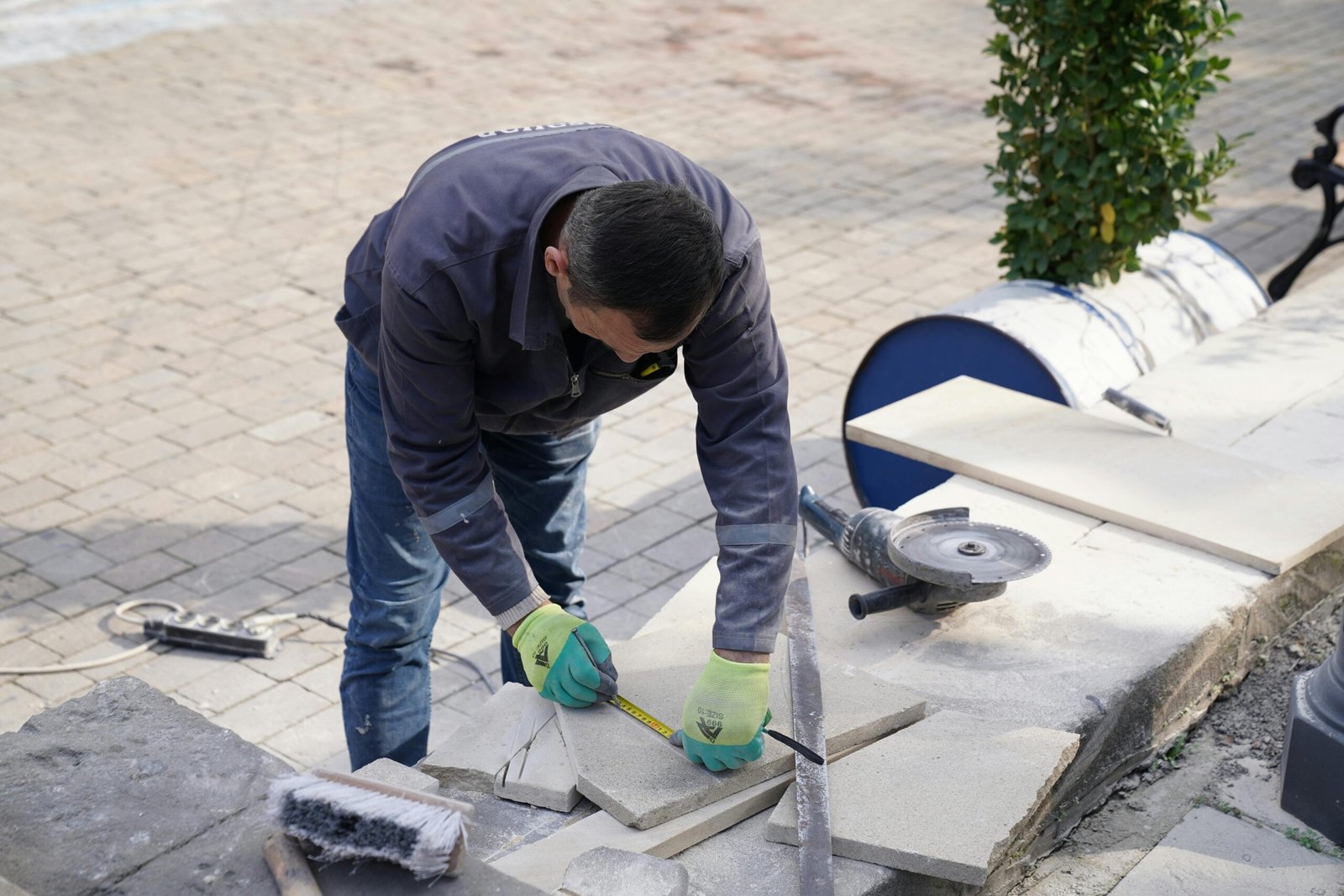 A construction worker measuring tiles outdoors with precision tools.